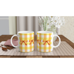 Pair of Yellow Gingham Bow Mugs with orange ribbons on a checkered tablecloth.