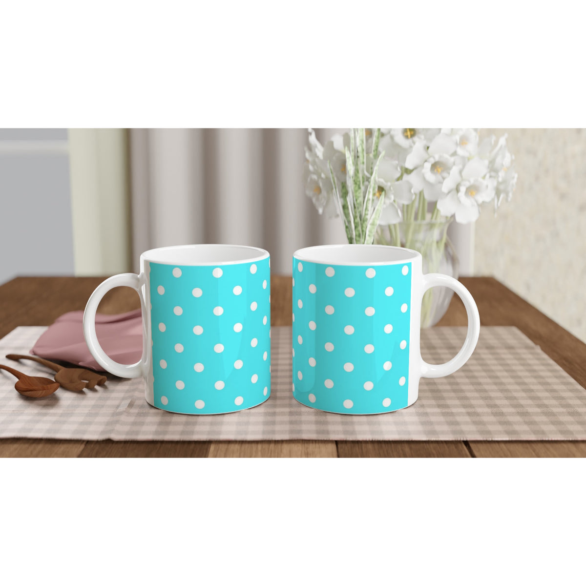 Aqua blue and white polka dot ceramic mugs with cute retro design sitting on a checkered placemat next to wooden spoons.