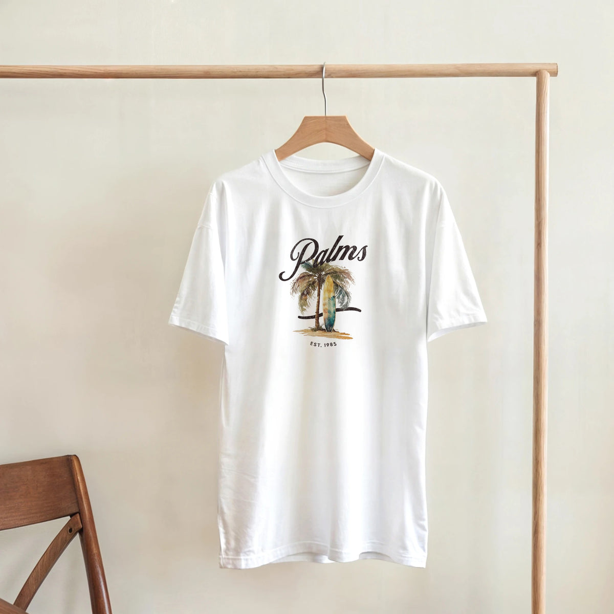 White women's palm tree graphic T-shirt with a soft cotton blend, crew neck, short sleeves, hanging on a wooden rack.