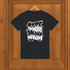 Black t-shirt with white text on a wooden hanger against a wooden background