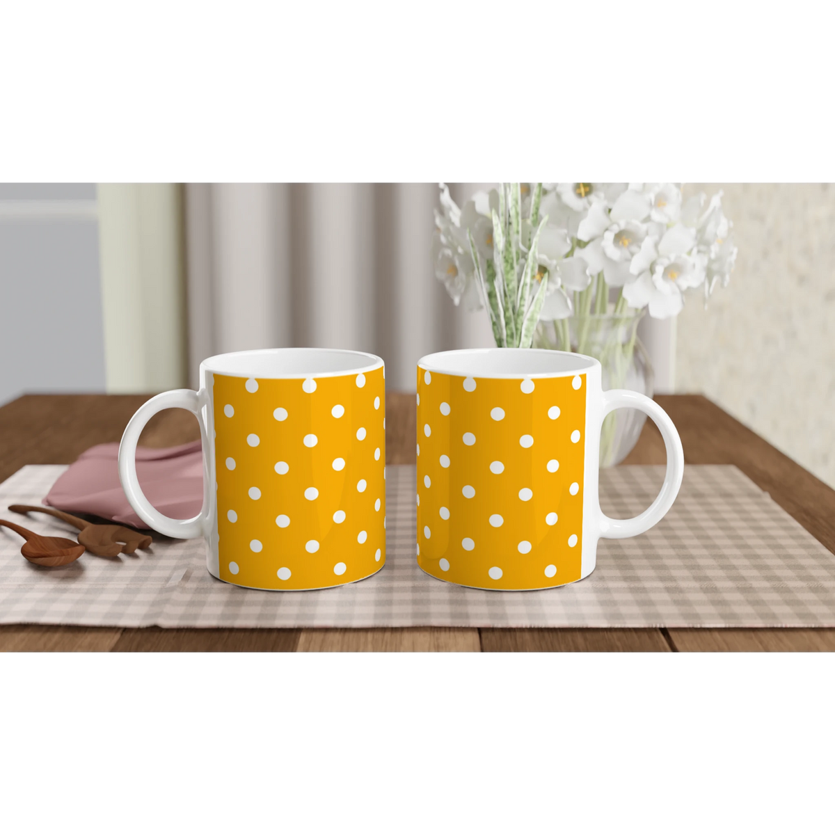 Pair of orange and white polka dot ceramic mugs sitting on a checkered placemat with wooden spoons and white flowers nearby.