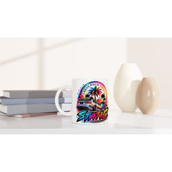 White petrolhead mug featuring colorful car and palm tree static design on a desk with books.