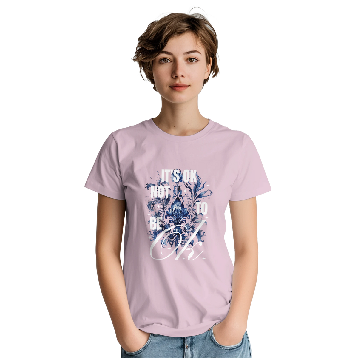Woman wearing pale pink cotton-blend tee with blue floral graphic and It's OK Not To Be OK slogan.