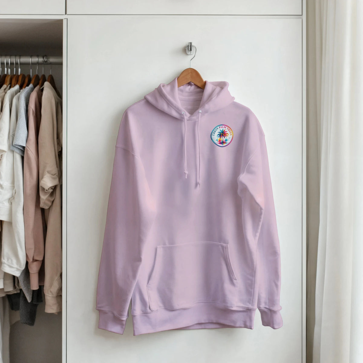 Lavender hoodie featuring a colorful circular Urban Palm Trees logo on the chest, hanging on a wooden hanger in a closet.