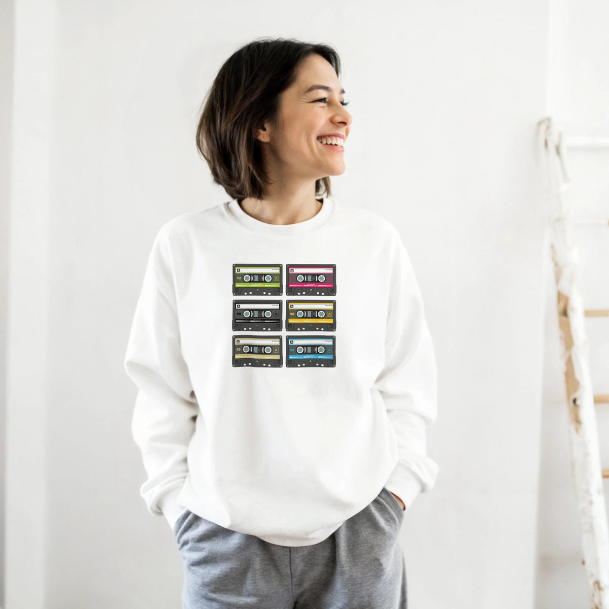 White vintage sweatshirt featuring a grid of six colorful retro cassette tape graphics for 90s music nostalgia.