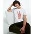 Man wearing white heavyweight cotton blend Peace graphic T-shirt with red typographic peace sign hand, seated.
