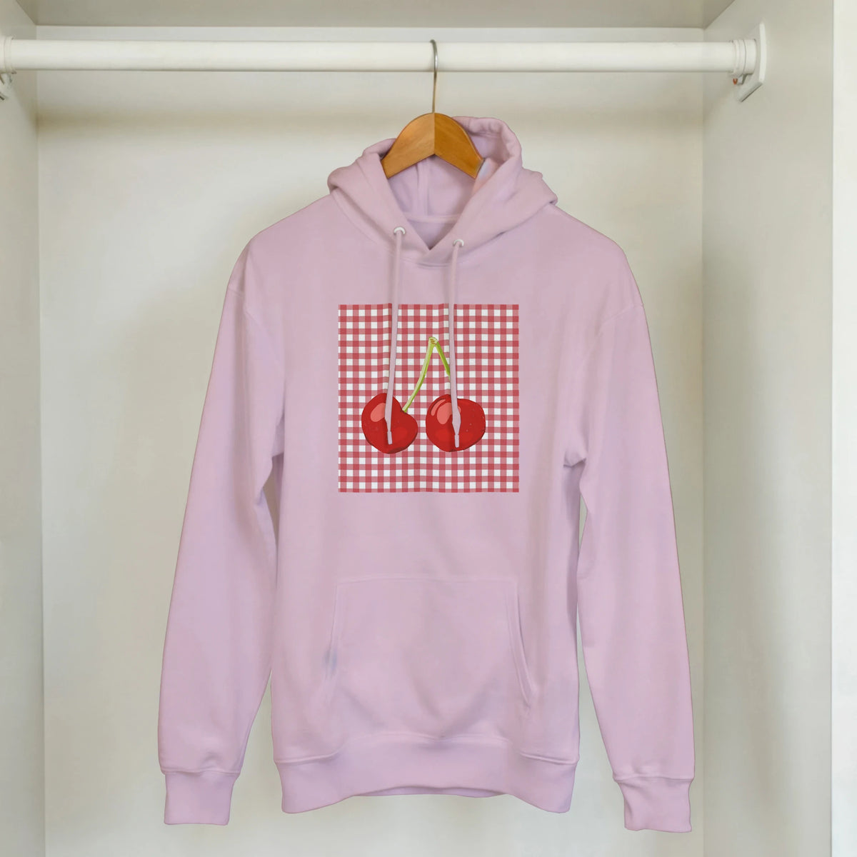 Pink retro cherry gingham hoodie for women with cherry graphic, hanging on a wooden hanger.