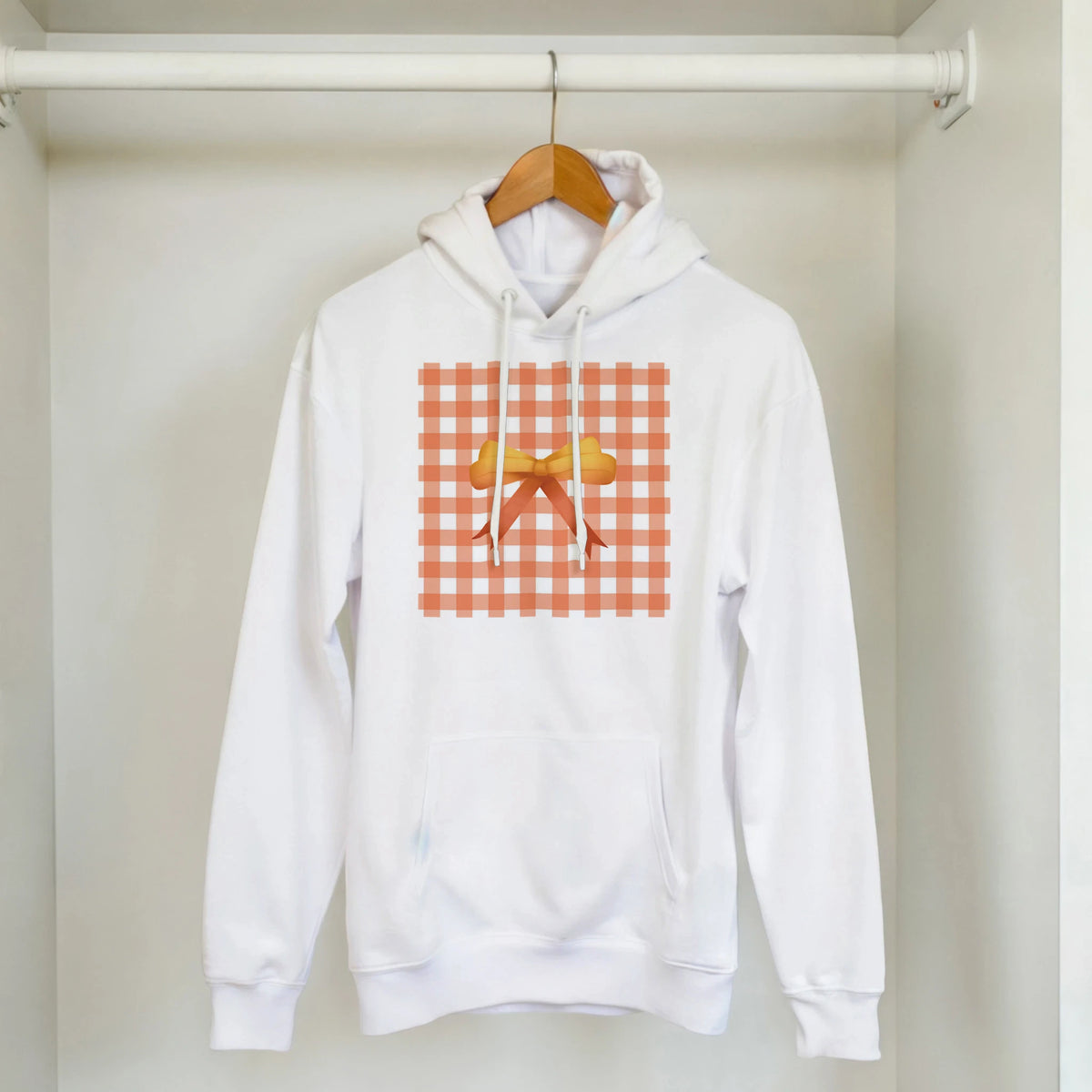 White pullover hoodie featuring an orange gingham square print with a central yellow bow for a cute coquette aesthetic streetwear look.