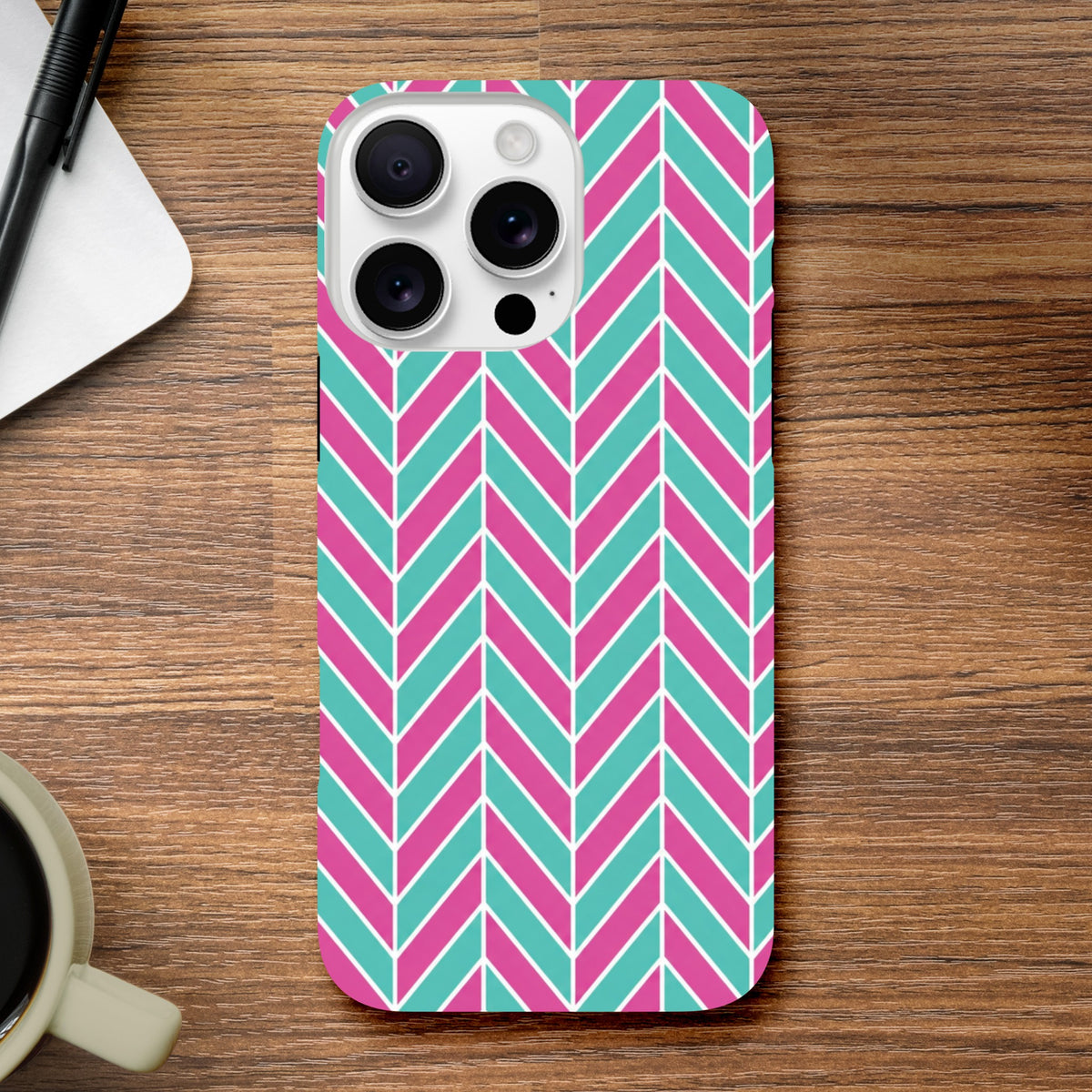 Pink and turquoise herringbone iPhone case on wooden desk. Geometric color-blocked phone cover with tough protective design for通勤 and home office.