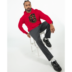 Man wearing red Grizzly Bear Hoodie with graphic design, seated on white stool, grey pants, black loafers.