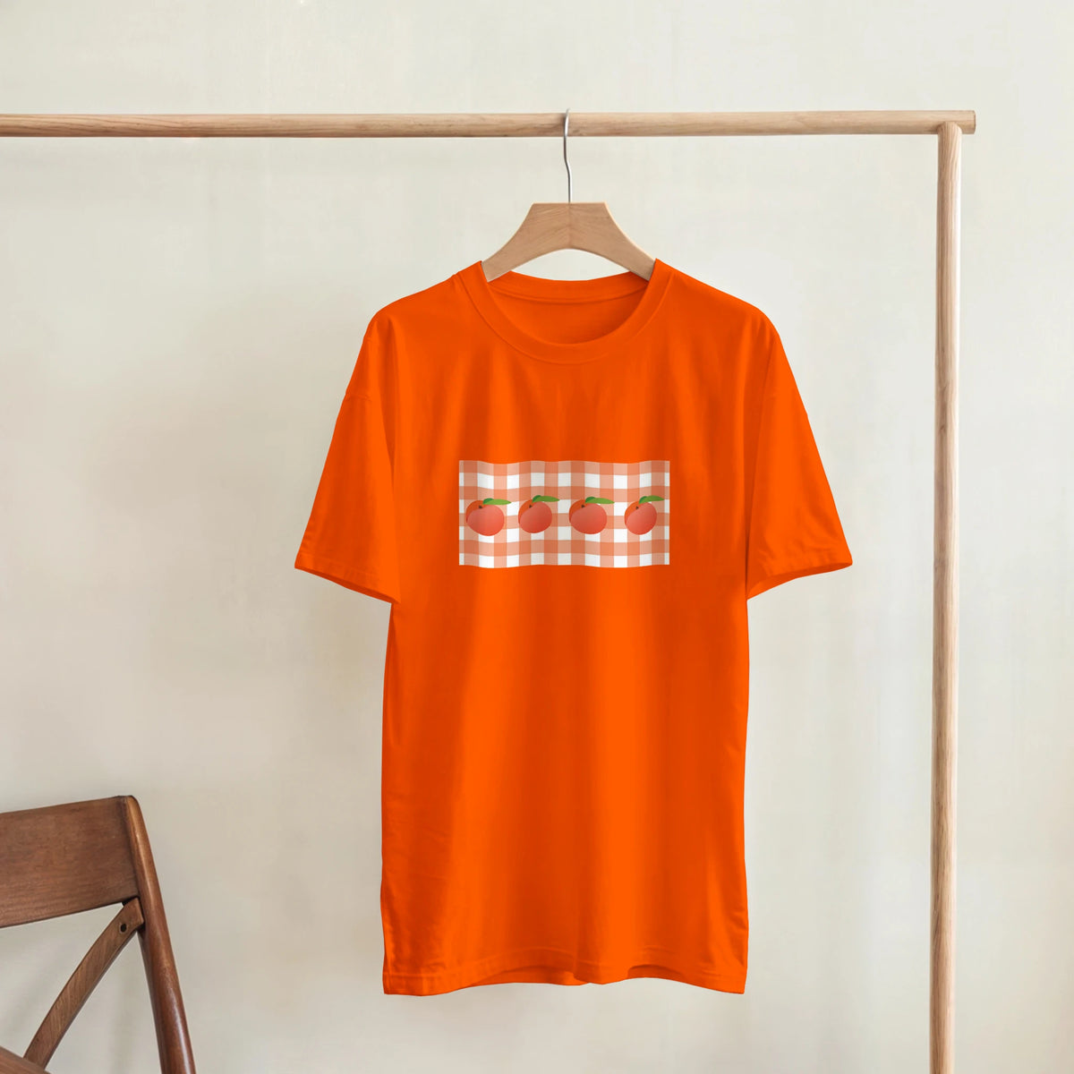 Orange women's T-shirt with a peach graphic on a gingham-check square.