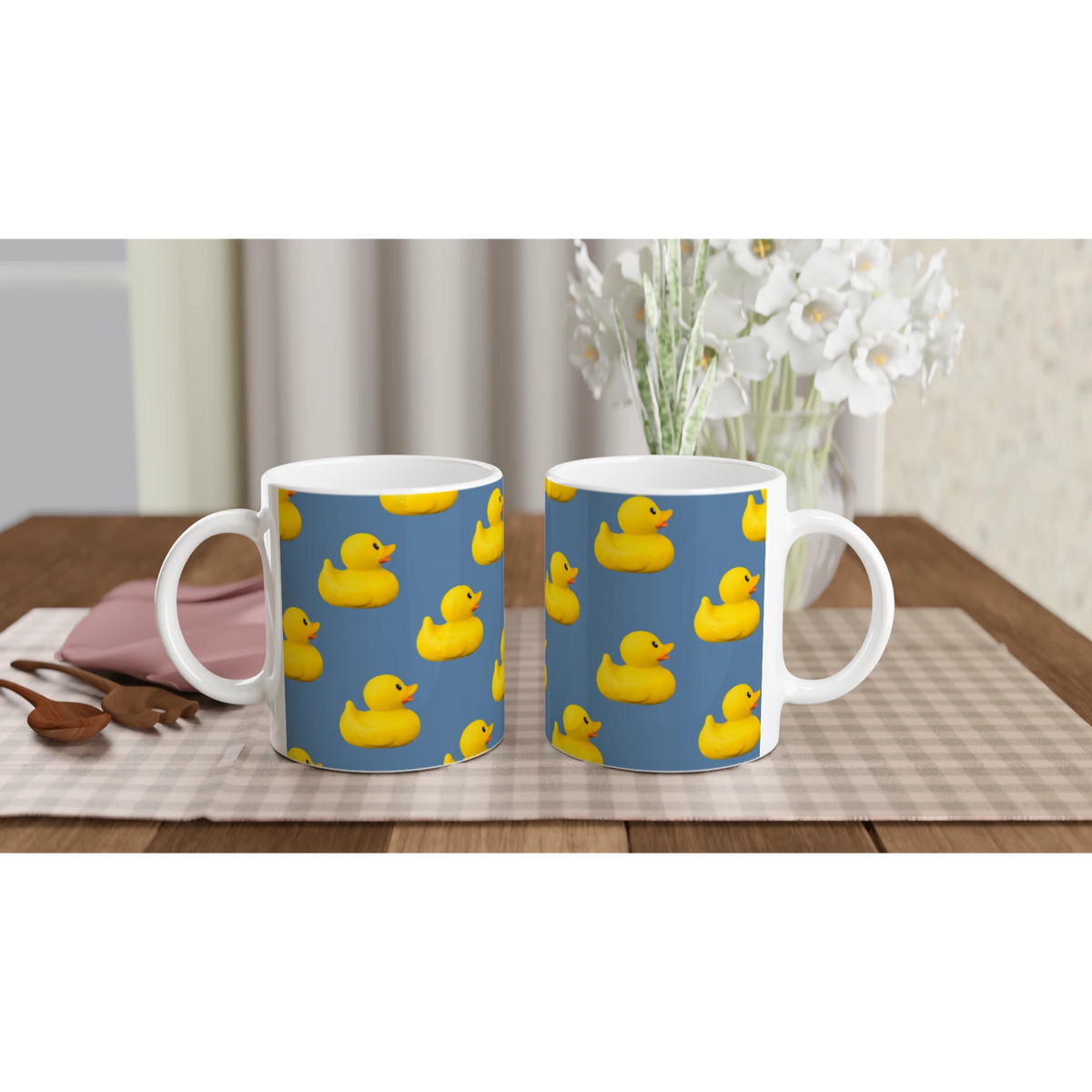 Two ceramic mugs with yellow rubber ducks printed on a blue background on a table.