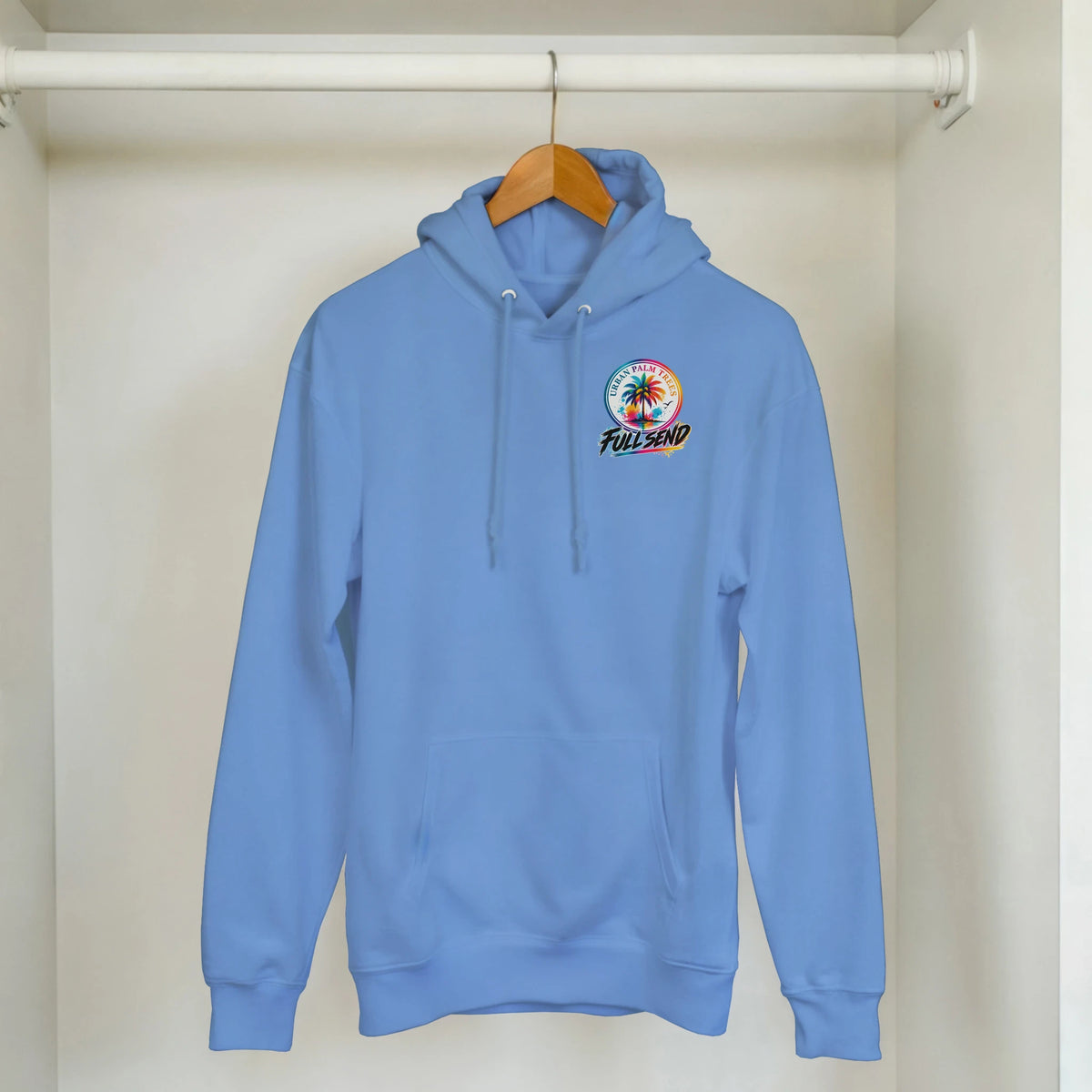 Light blue streetwear hoodie with colorful Urban Palm Trees Full Send graphic, front pouch pocket, and drawstrings hanging on a wooden hanger.