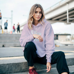 Woman wearing lavender Stay True hoodie with front pocket on urban steps.