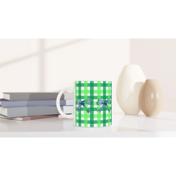 Green gingham bow mug with purple ribbons on a desk beside books.