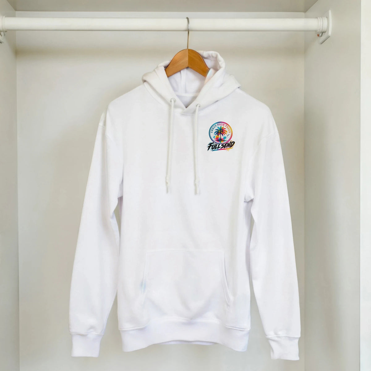 White streetwear hoodie with colorful "Full Send" palm tree graphic on chest, hanging in a closet.