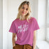 Woman wearing pink 'Wild and Free' slogan T-shirt, retro streetwear vibe by a bright window.