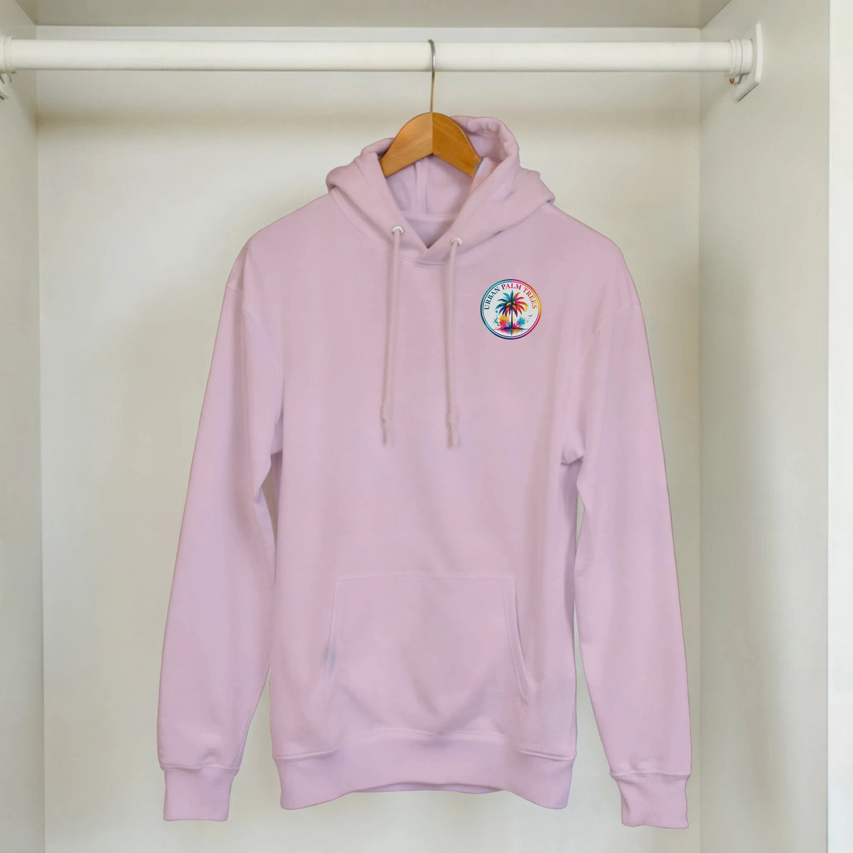 Pink hoodie with colorful Urban Palm Trees logo patch hanging in closet. Retro tropical graphic sweatshirt with kangaroo pocket.