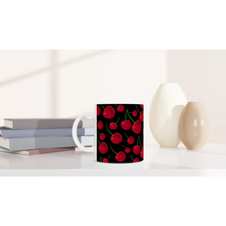 Vintage aesthetic ceramic coffee mug featuring a black background with a bright red cherry fruit pattern, sitting on a white desk.