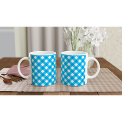 Blue gingham ceramic mugs on a checkered table with a vase of white flowers in the background.