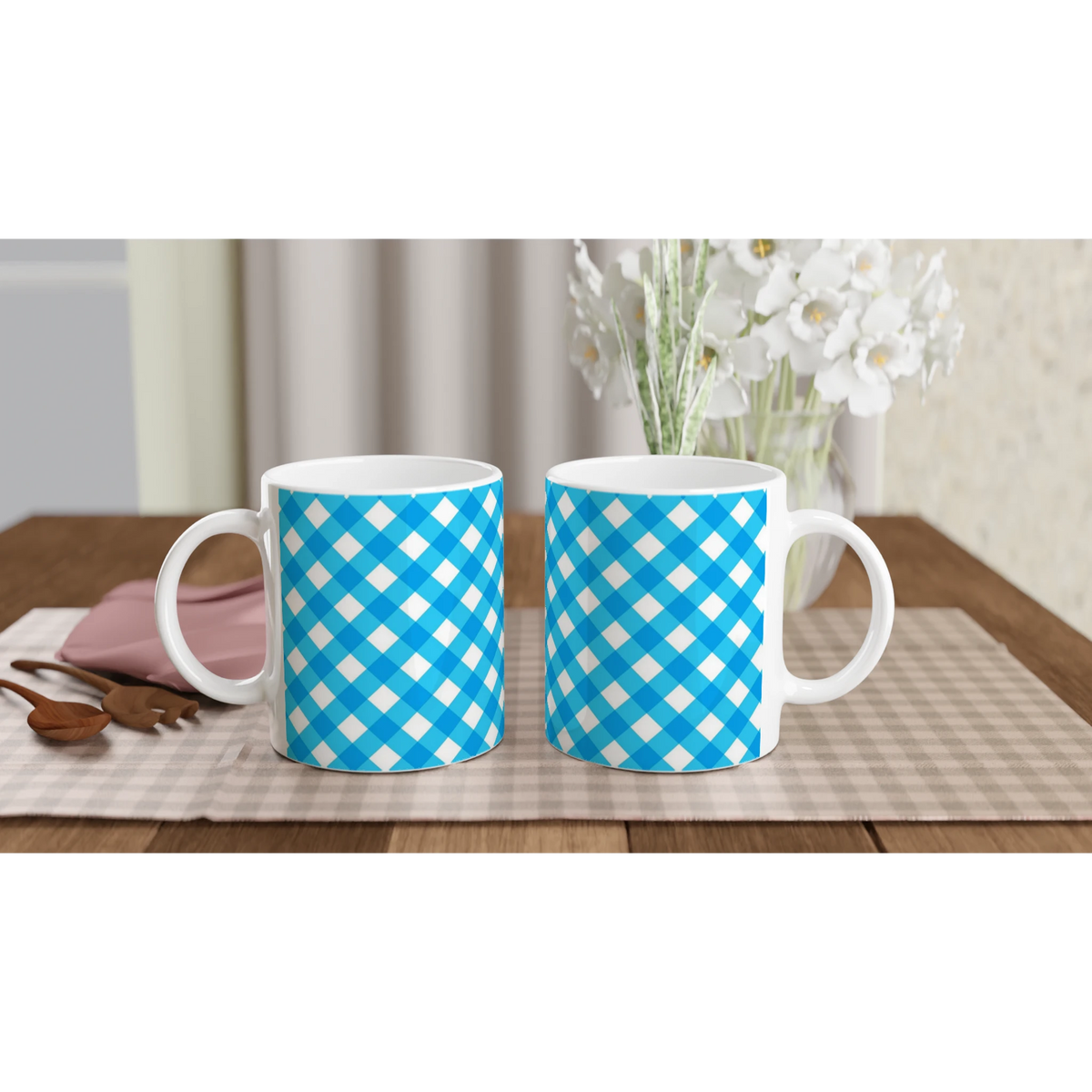 Blue gingham ceramic mugs on a checkered table with a vase of white flowers in the background.
