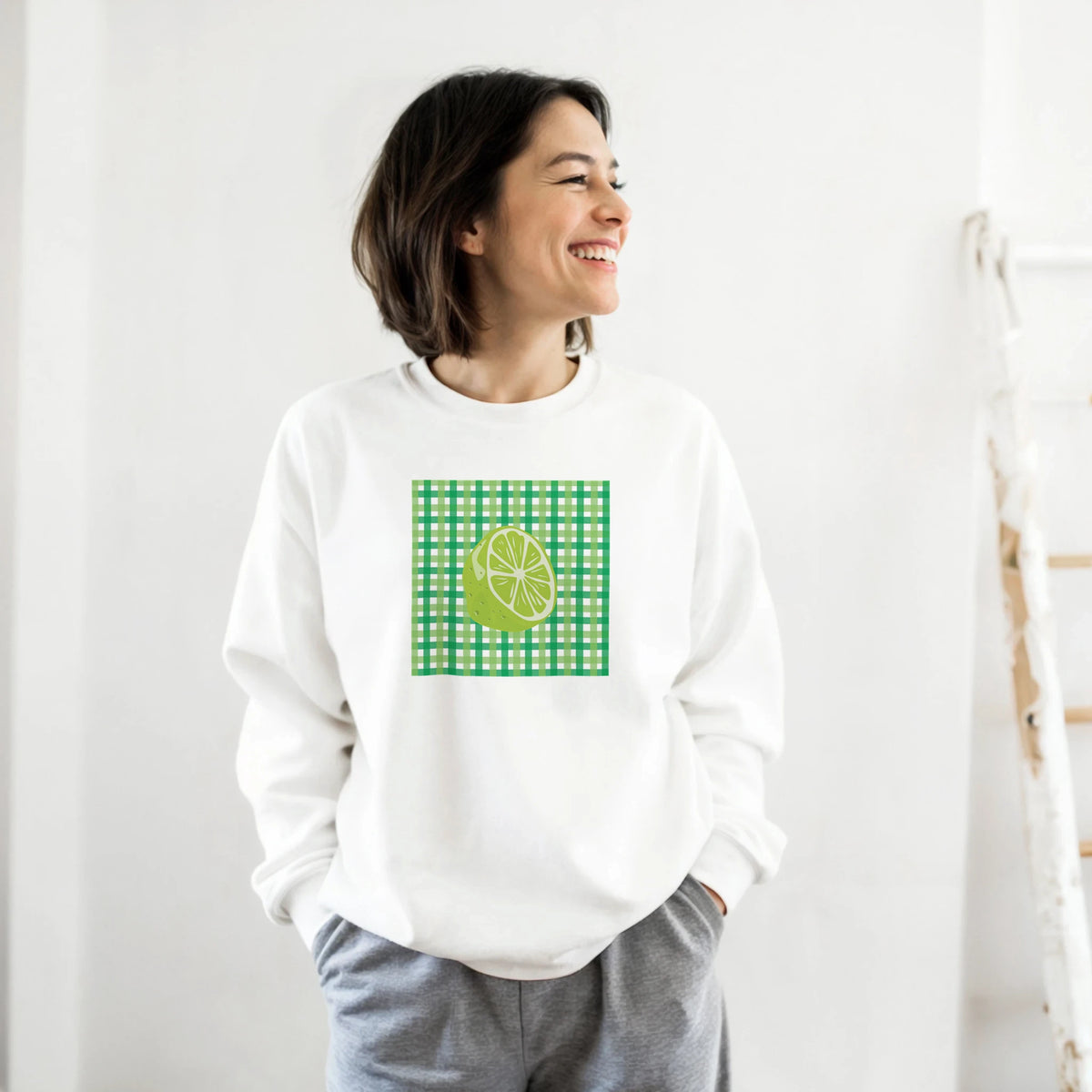 Smiling woman wearing a white sweatshirt with a lime graphic on green gingham.