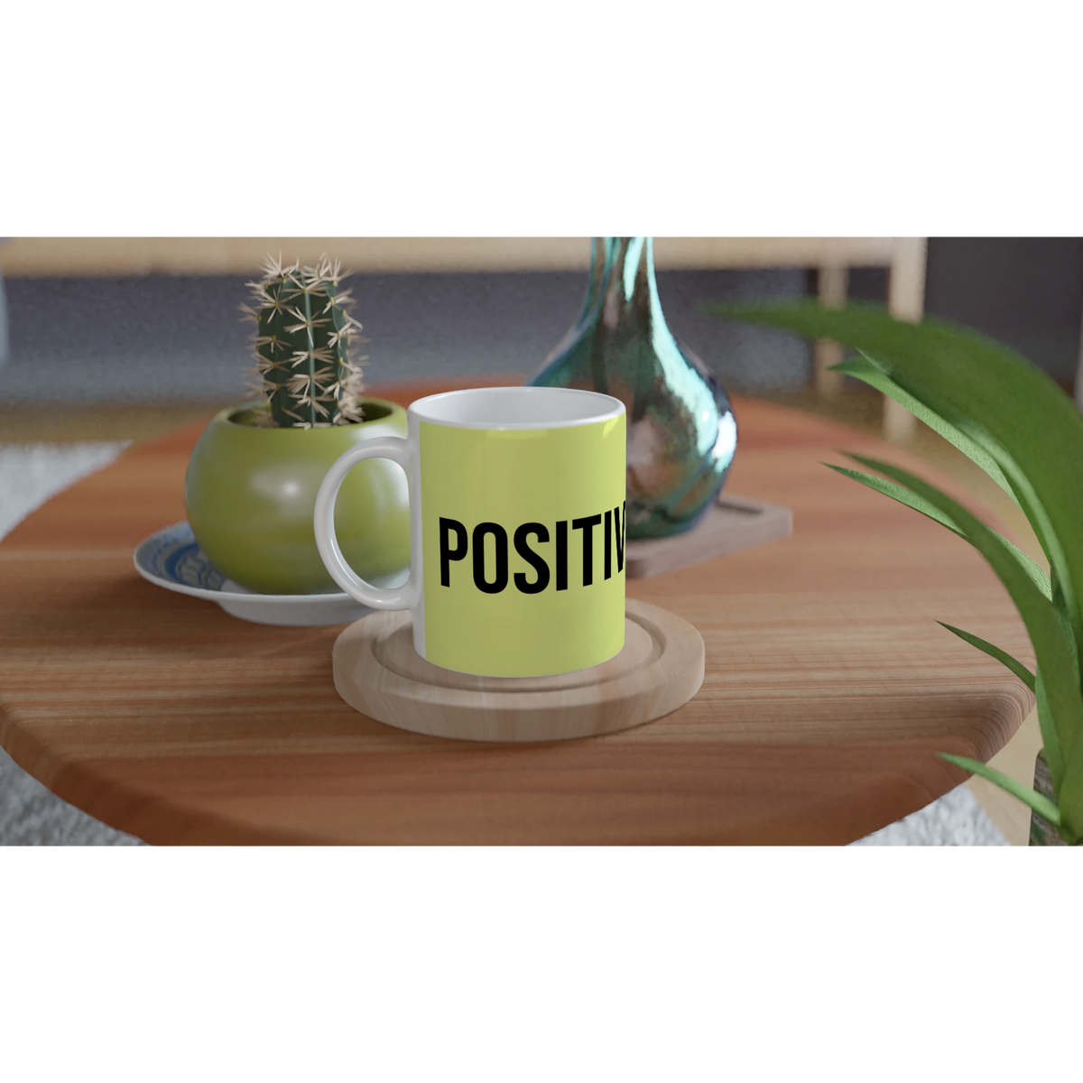 Light-green mug with bold POSITIVE text sits on a wooden table beside a small cactus.