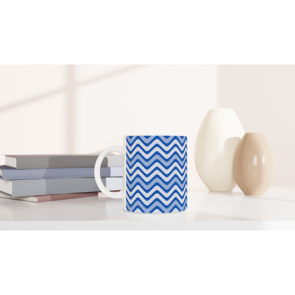 Blue wavy stripe ceramic mug on a white desk beside books and vases. Retro geometric coffee cup for home or office.