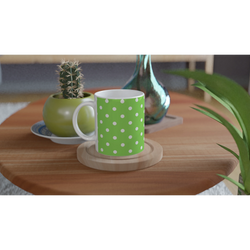 Green and white polka dot ceramic mug on a wooden coaster, featuring a vibrant spotty motif next to a small cactus.