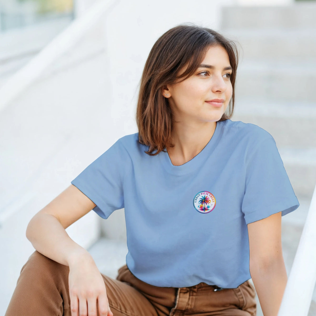 Woman wearing a blue retro graphic tee with a colorful circular palm tree logo on the chest.