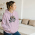 Woman wearing lavender You Matter hoodie with floral graphic, front pocket, and drawstring hood.