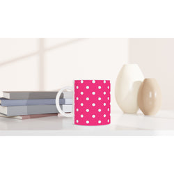 Retro hot pink ceramic mug with white polka dots on a white desk beside stacked books and minimalist vases.