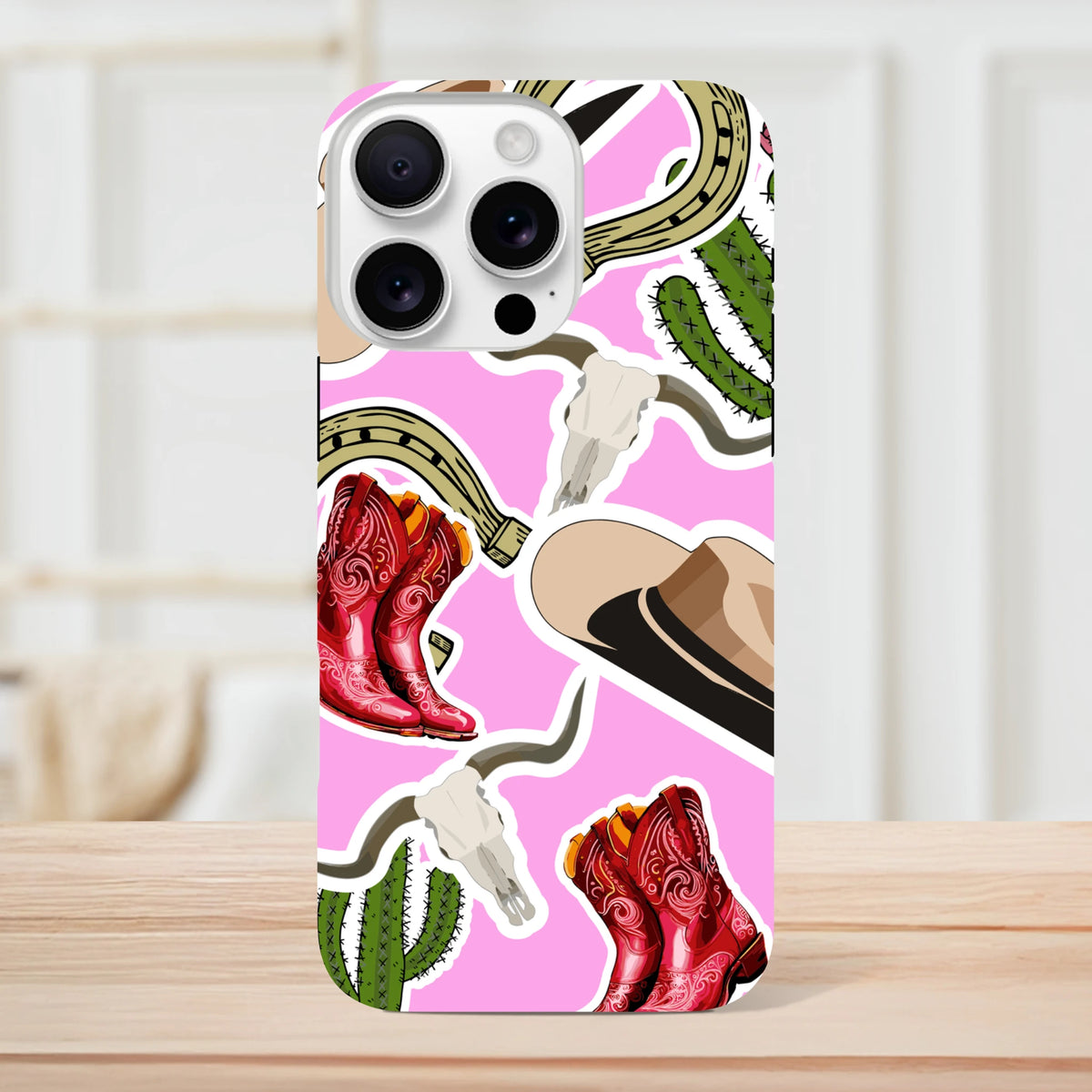 Pink western iPhone case featuring red cowboy boots, cactus, horseshoe, and cow skull motifs on a vibrant pink background.