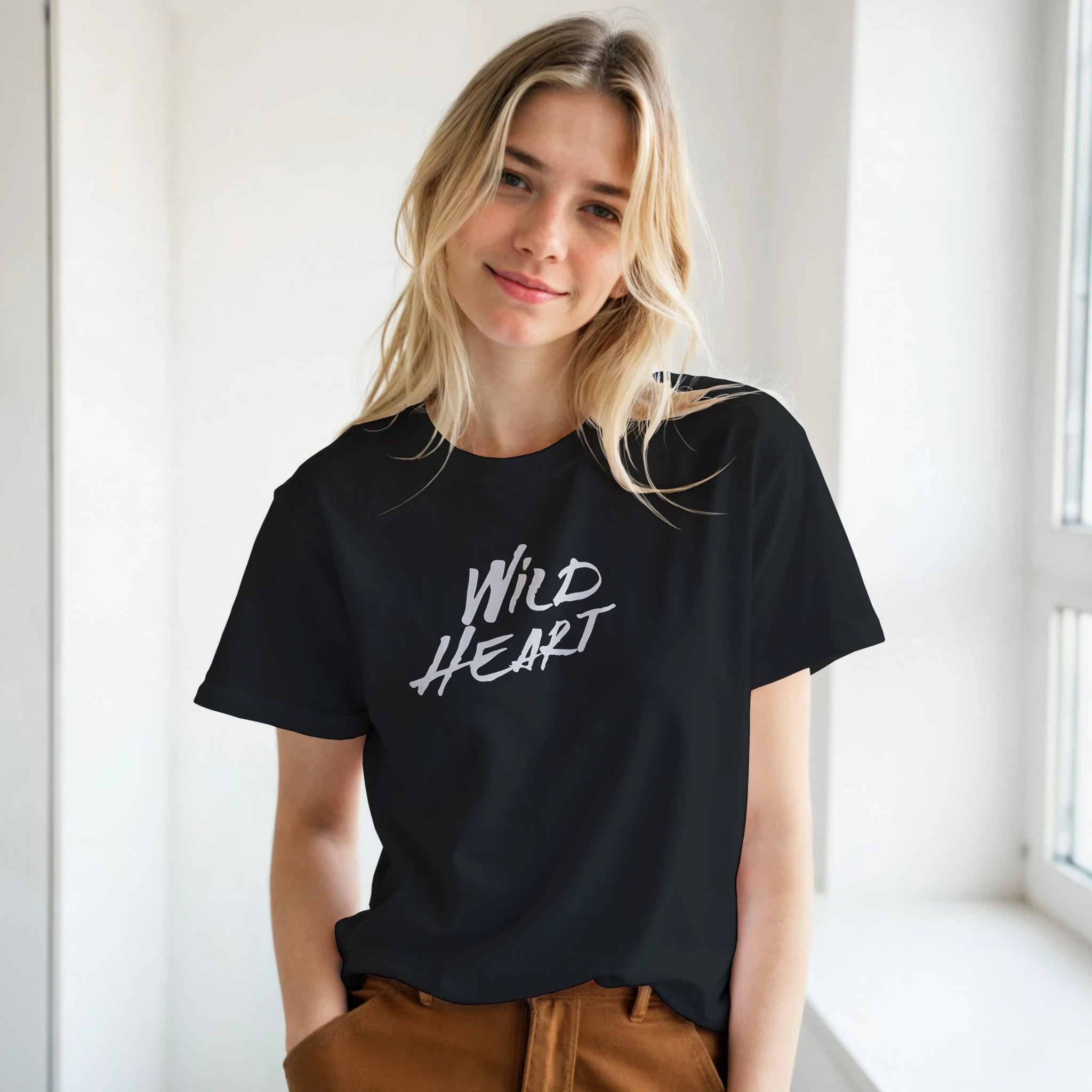 Female model wearing black Wild Heart T-Shirt with retro slogan in a sunlit corridor.