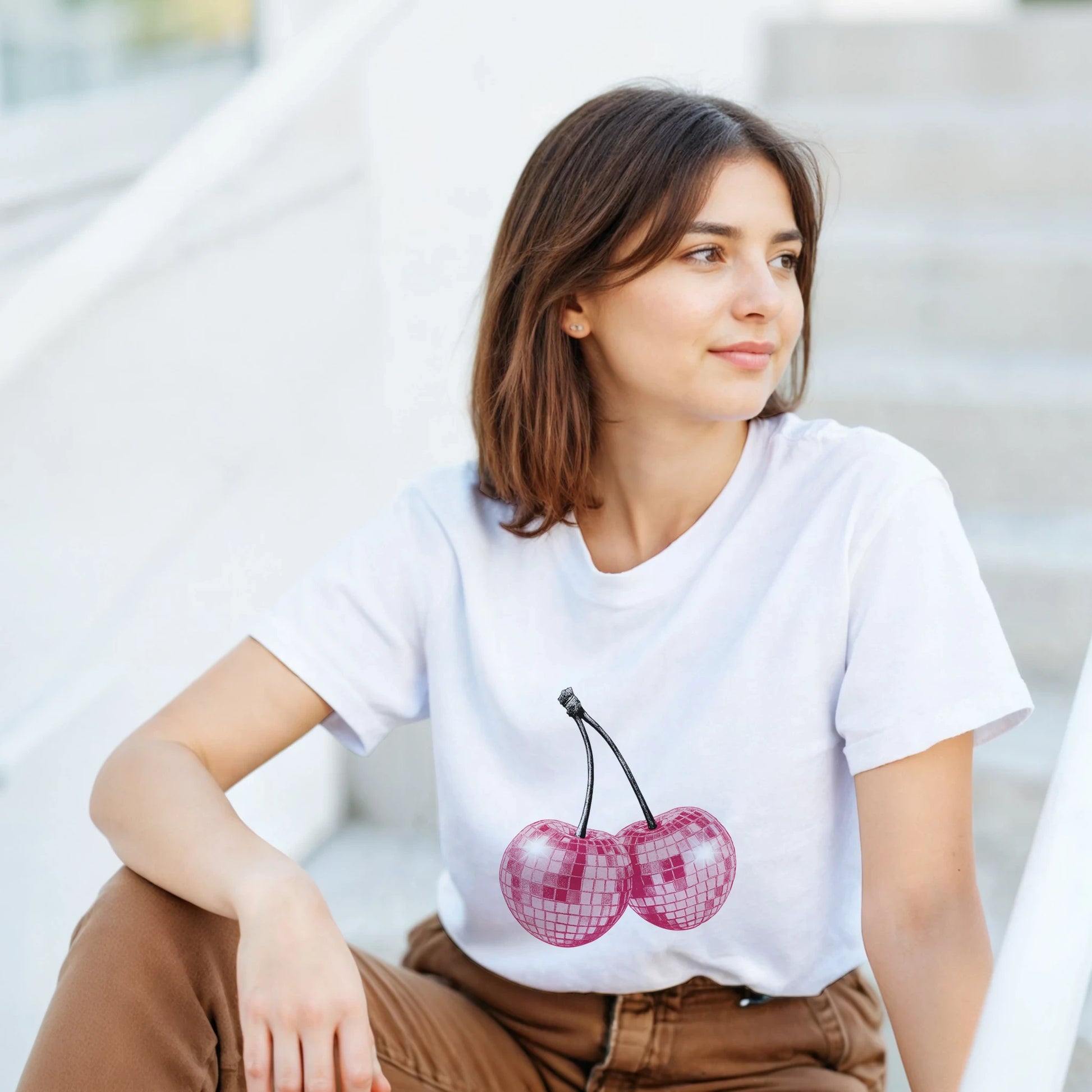 Woman wearing white Glitter Ball Cherries T‑Shirt with pink cherry graphic on soft cotton blend tee.