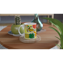 Vibrant ceramic coffee mug featuring banana, pineapple, and orange illustrations on a wooden table with a cactus.