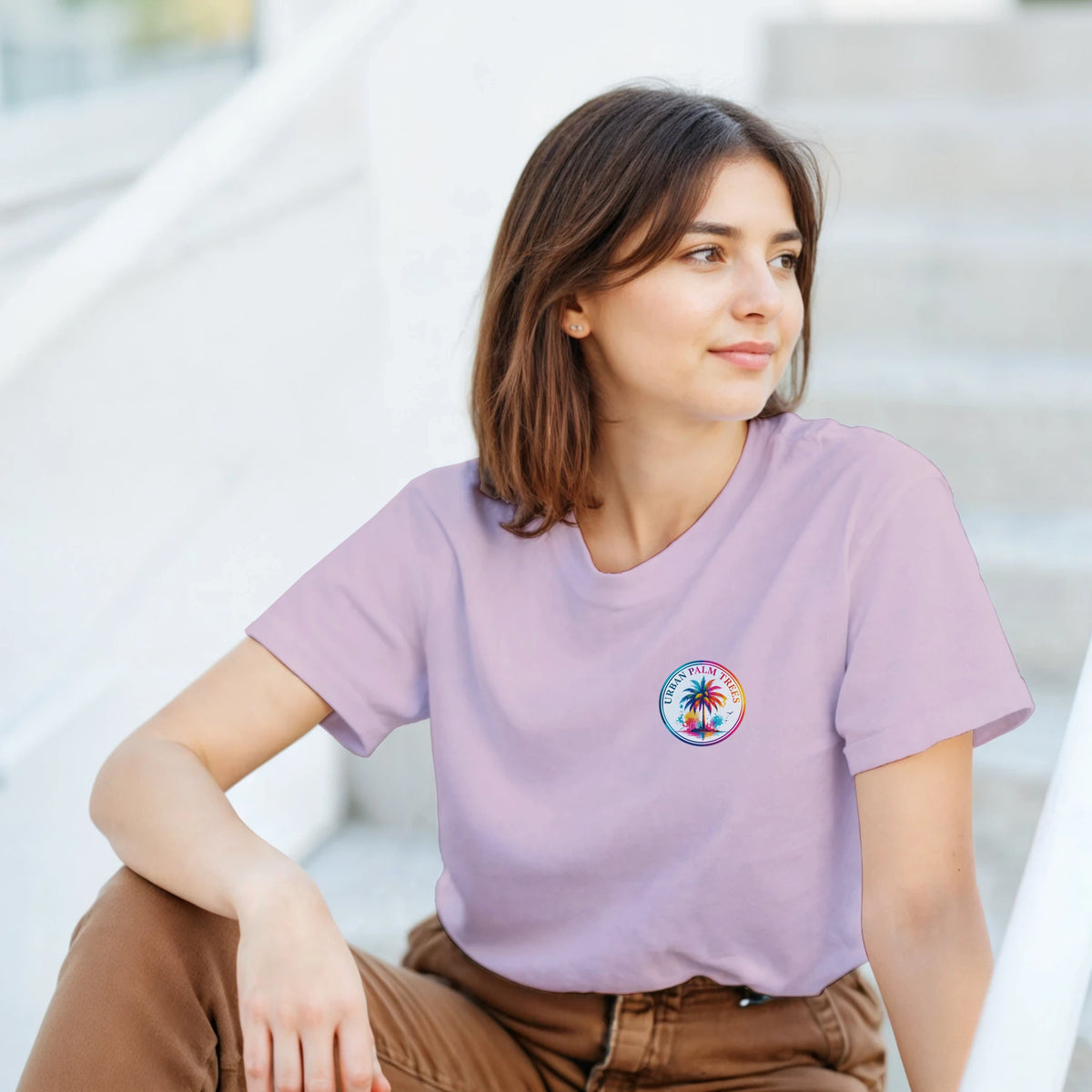 Woman wearing a lavender graphic tee with a small retro palm tree circular logo on the chest.