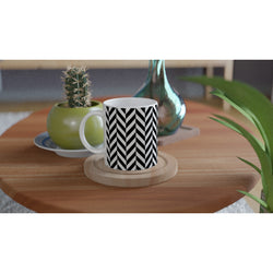 Black and white herringbone ceramic mug on wooden coaster beside cactus on natural wood table