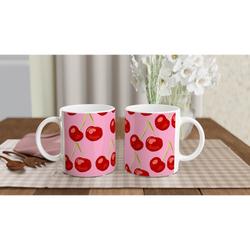 Two pink cherry-pattern ceramic mugs with white handles on a checkered table, cozy kitchen scene.