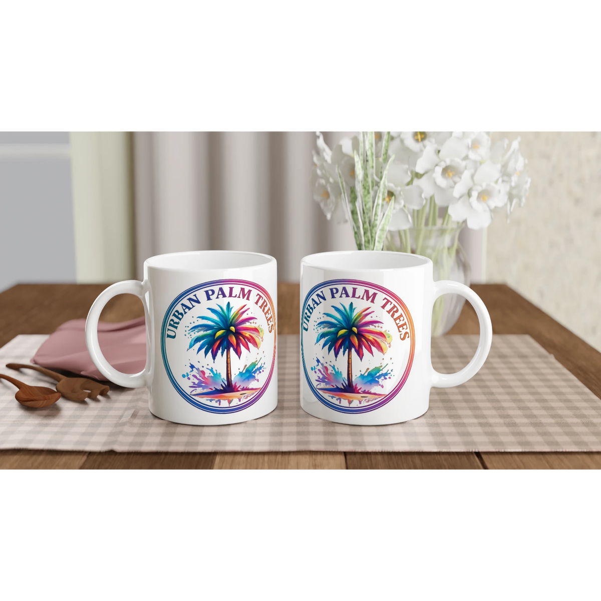 Two white ceramic Urban Palm Trees mugs with colorful palm-tree artwork on a checkered table.