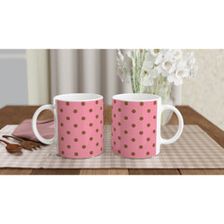 Two pink ceramic mugs with brown polka dots sit on a checkered mat next to wooden spoons and white flowers.