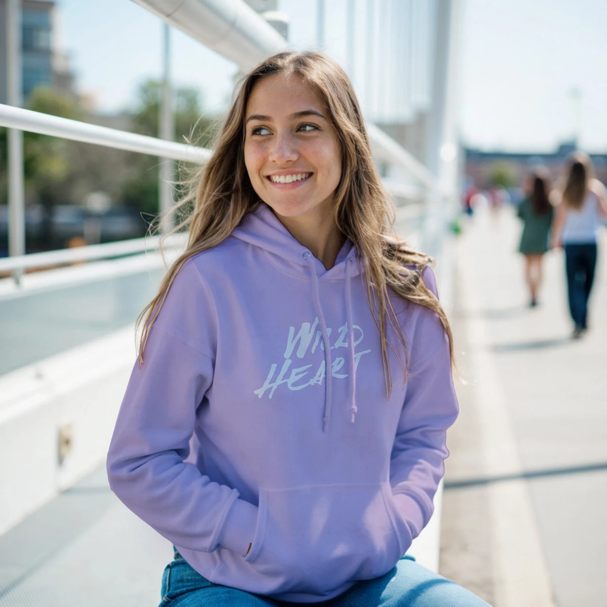 Smiling woman in a lavender Cute Wild Heart hoodie, a cozy slogan top for women, on an urban walkway.
