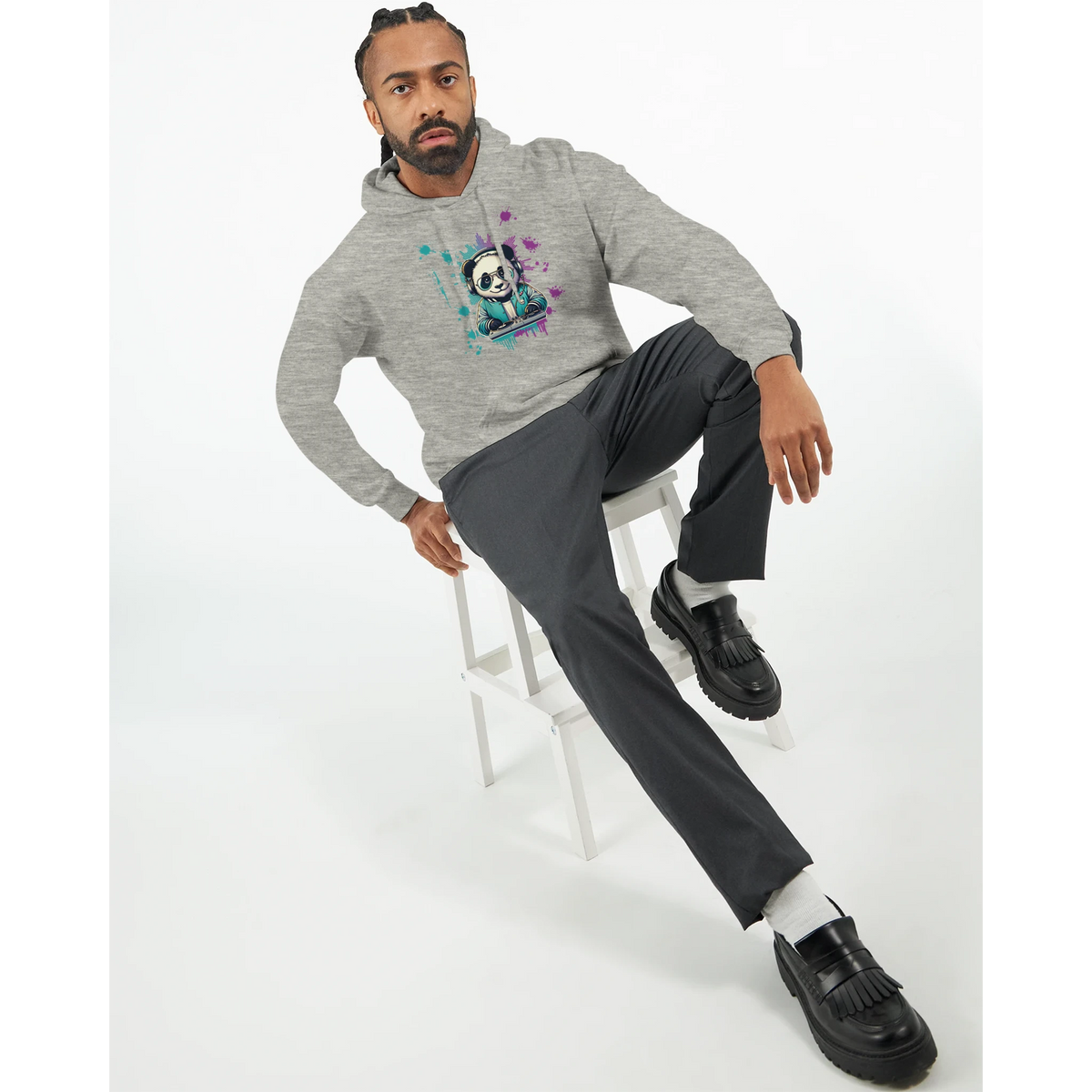 Man modeling Panda DJ graphic hoodie in heather grey with colorful panda print, sitting on a white stool.