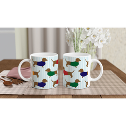 Two dachshund-pattern ceramic mugs with blue stripes, set on a table with a vase of white flowers.