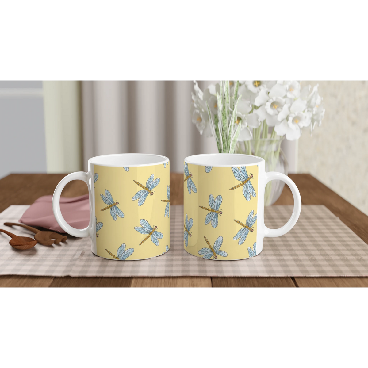 Two yellow dragonfly ceramic mugs with blue dragonfly patterns on a wooden table.