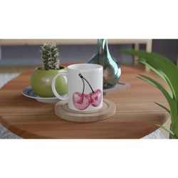 Cute Glitter Cherries retro aesthetic coffee cup on a wooden table, with cactus and vase nearby.