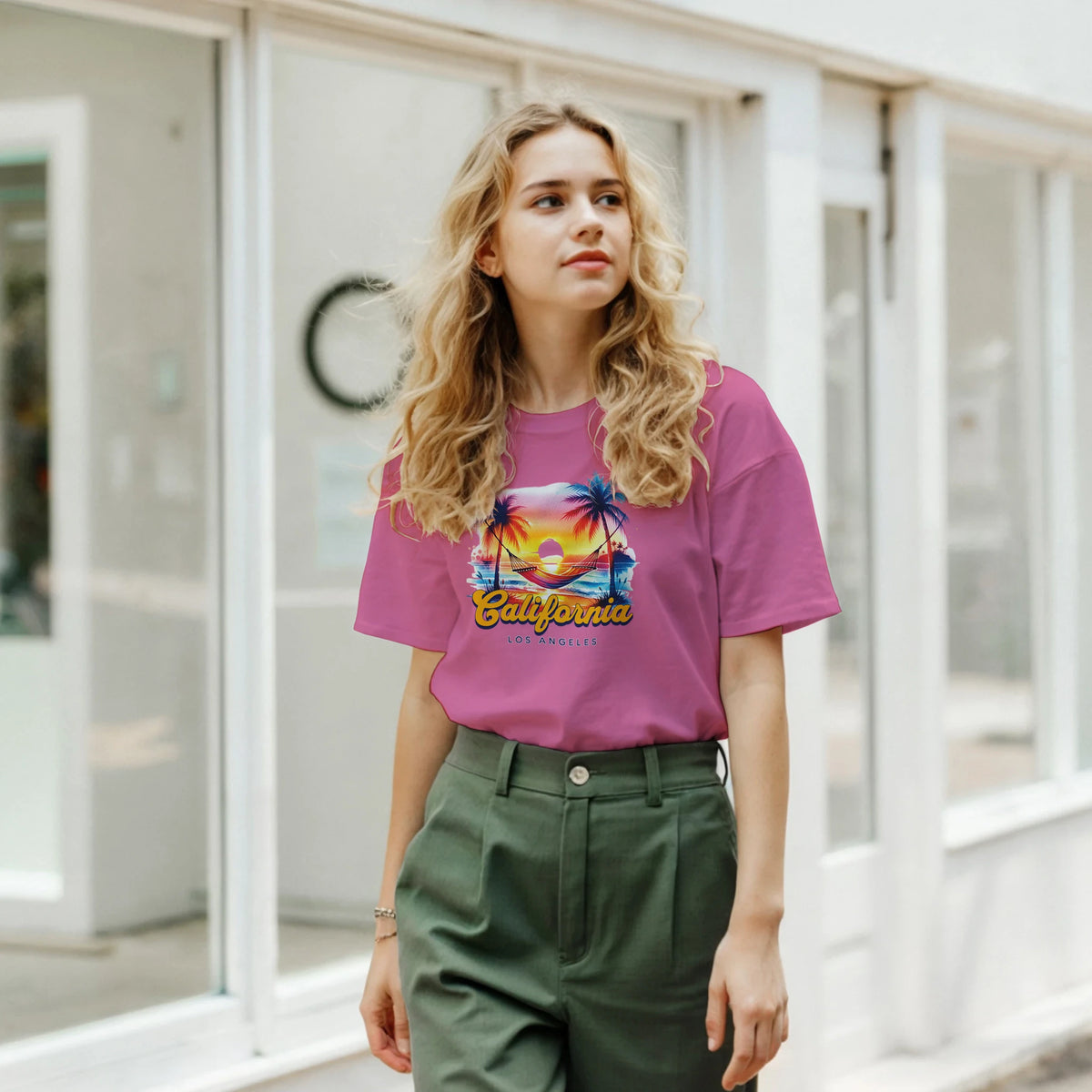 Woman wearing pink retro California T-shirt with palm tree sunset graphic outdoors.