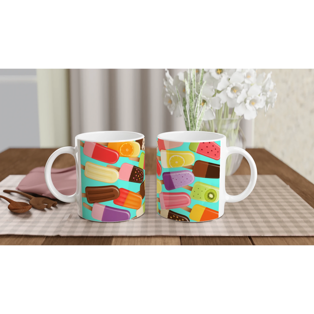Two ceramic mugs featuring a retro colourful popsicle pattern on a turquoise background, set on a checkered placemat with wooden spoons.