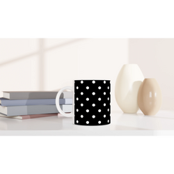 Black ceramic mug with white polka dots on a white desk beside books and vases. Vintage spotty coffee cup for daily brews.