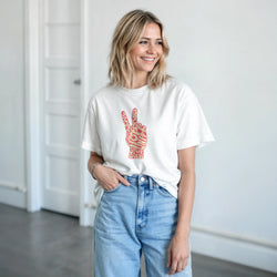 White crewneck tee featuring a retro pink and yellow peace sign graphic made of typography, paired with blue jeans for streetwear.
